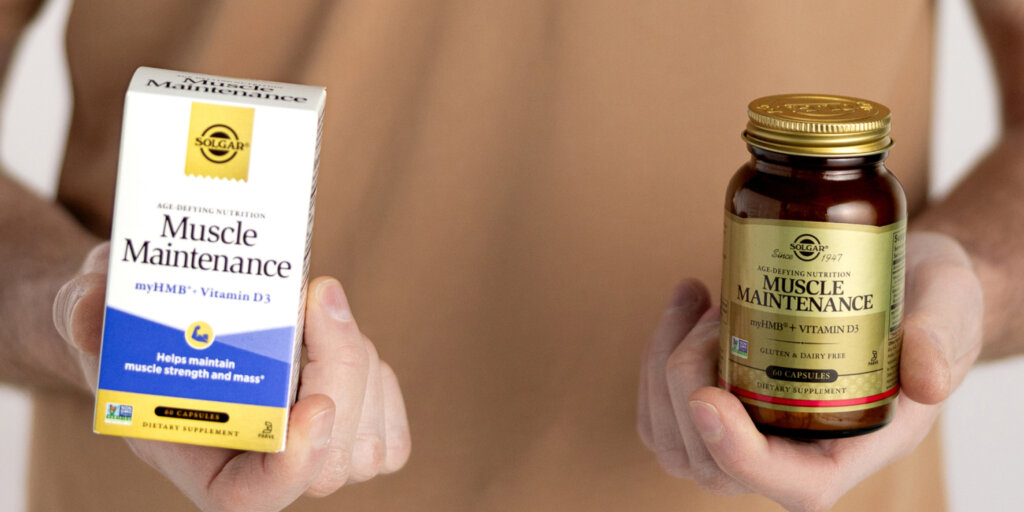 A closeup of a man holding a box of Solgar Muscle Maintenance in one hand, and a bottle of Muscle Maintenance in the other. 