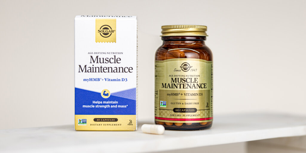 A box and amber glass bottle of Solgar Muscle Maintenance capsules. One capsule is out of the bottle and sitting on a marble countertop. 