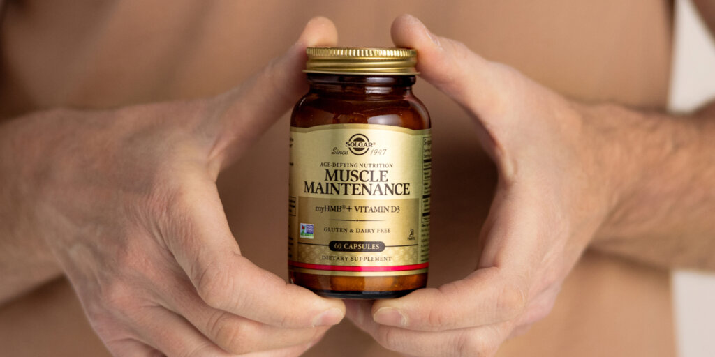 An amber glass bottle of Solgar Muscle Maintenance capsules held in a man's hands.