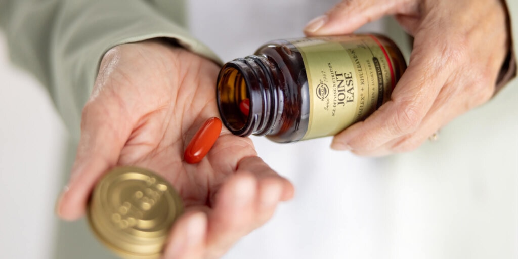 hands holding a amber glass bottle with a red capsule 