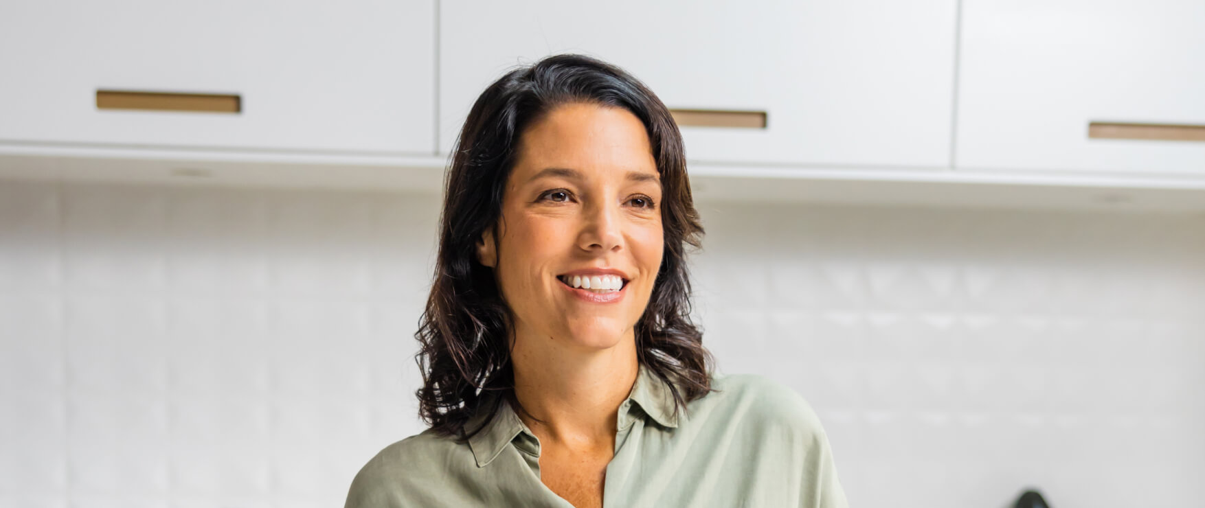 brunette woman in a white kitchen smiling